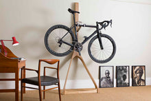 Load image into Gallery viewer, A living room with a Wishbone wall stand against the wall holding a black Colnago road bike