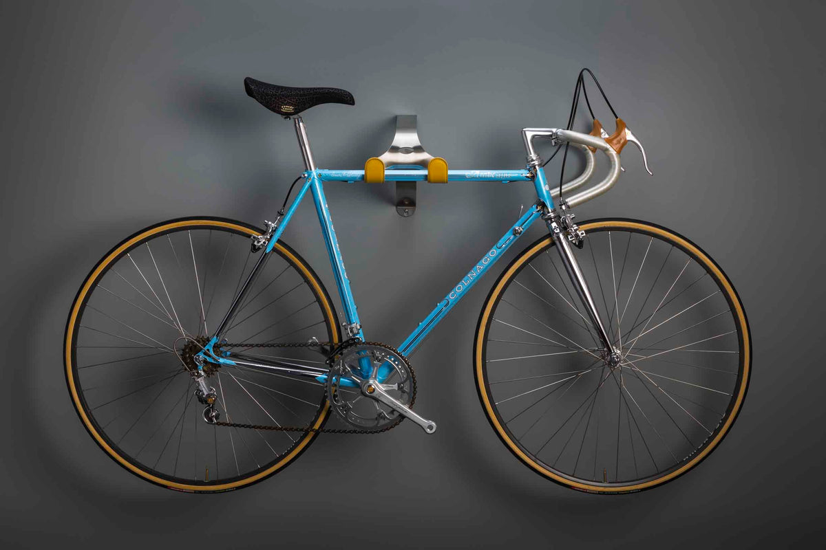 Classic blue Colnago road bike hanging on a Cactus Tongue SSL Roadie bike hanger with yellow leather sleeves.