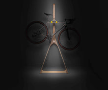 Load image into Gallery viewer, A titanium road bike hanging on a Cactus Tongue Wishbone wall stand dramatically lit by a beam of light from above
